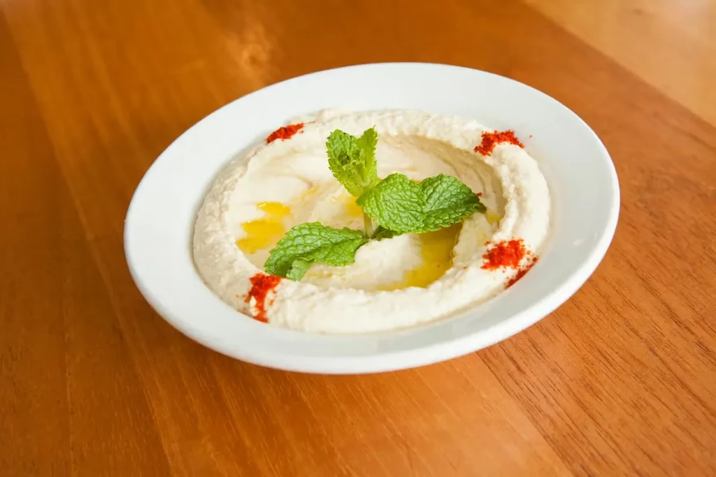 Creamy hummus bowl with olive oil, mint, and paprika on wooden table.