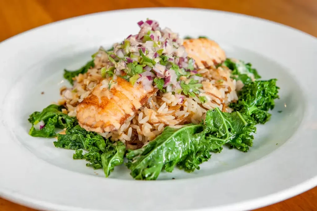 Plated grilled salmon, mixed rice, kale, and fresh herb salsa.