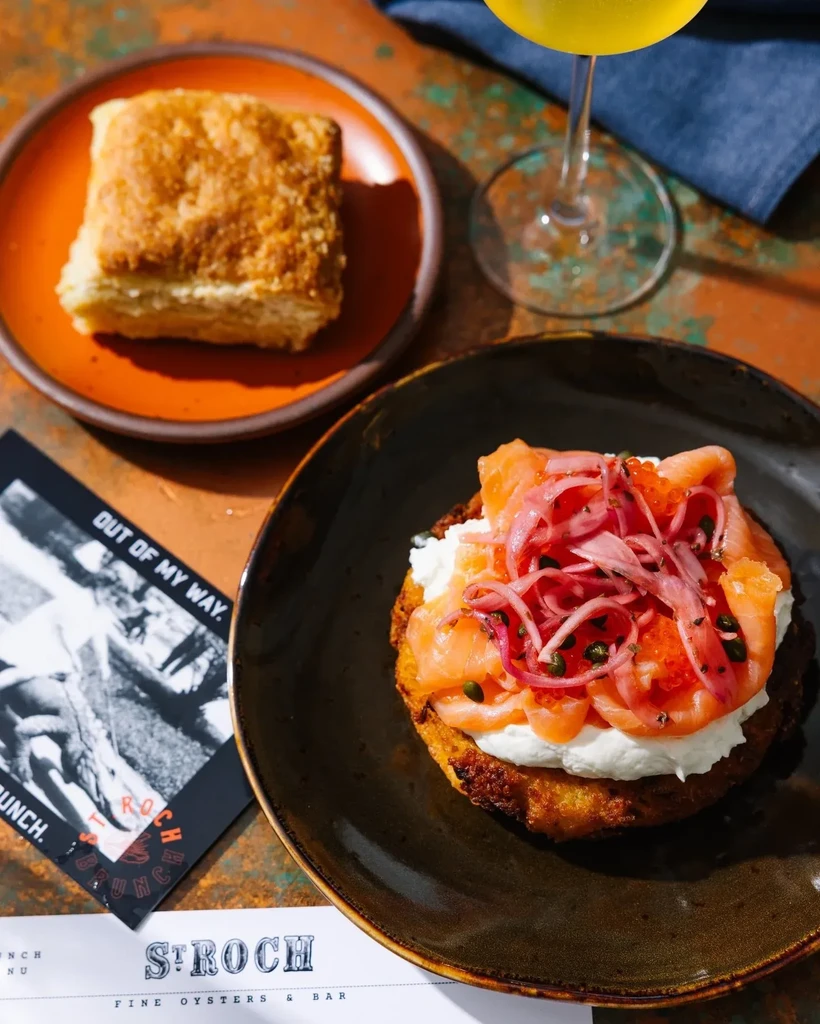 Restaurant table with smoked salmon, creamy spread, pickled onions, biscuit, and drink.