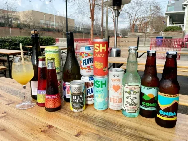 Various bottled and canned beverages and a cocktail on an outdoor table.