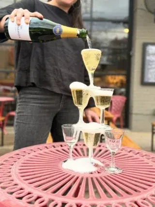 A person pours champagne into a cascading champagne tower outdoors.