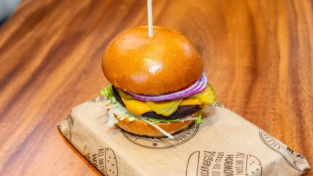 Gourmet burger with brioche, cheese, onion, pickle, lettuce on wood.