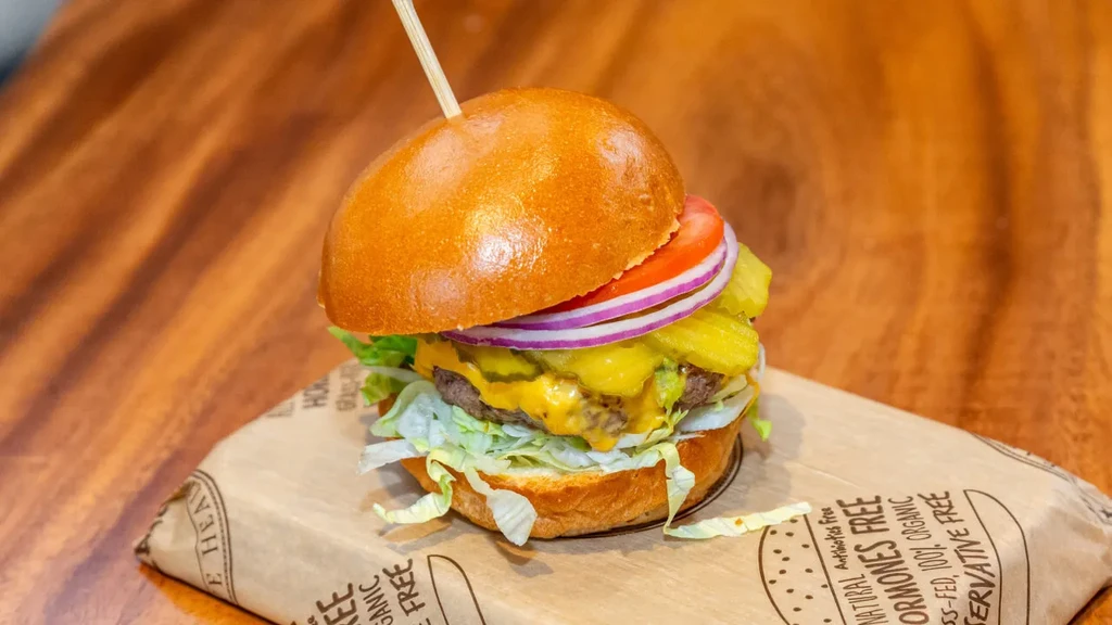 Burger with dill pickles on kraft paper stating "ORGANIC GRASS-FED."