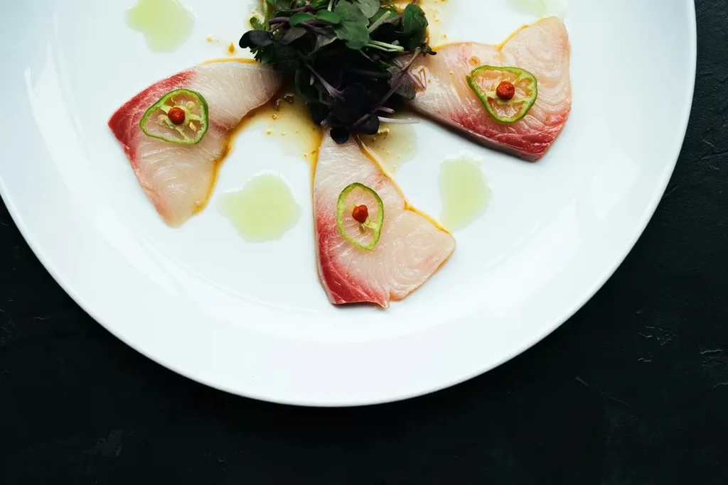 Sashimi-style raw fish slices with chili, microgreens, and sauces.