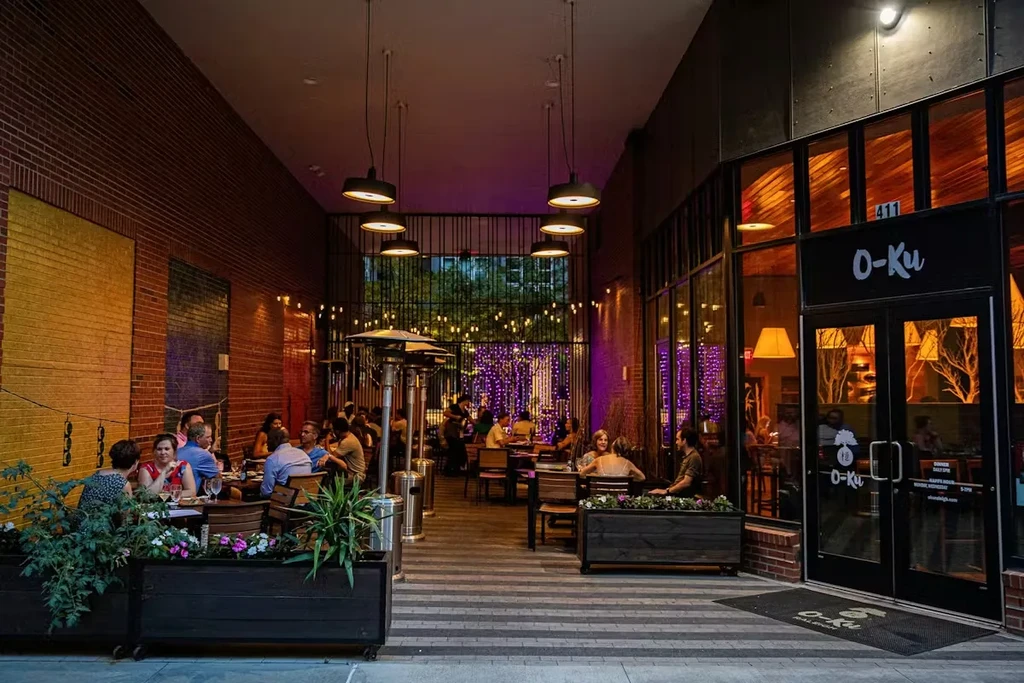 O-Ku restaurant's evening outdoor patio with diners, lights, and plants.
