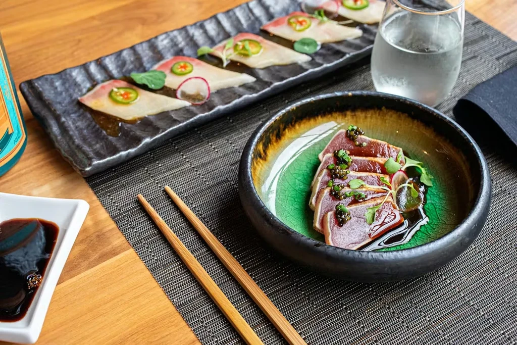 Japanese sashimi and seared tuna dishes with chopsticks on a table.