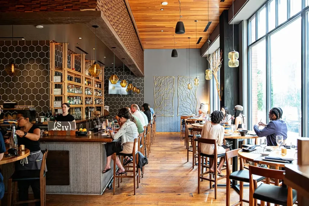 Modern restaurant with bar, dining area, warm wood, and abstract metal art.