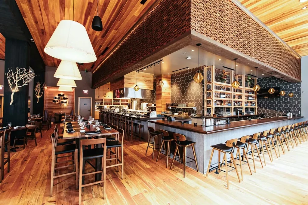 Modern restaurant interior with dark wood bar, wooden ceiling, pendant lights.