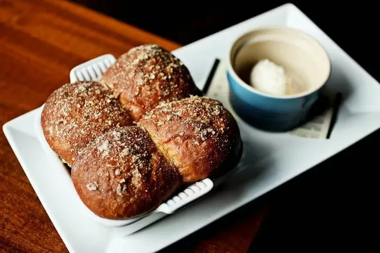 Four golden-brown rolls with coarse topping and butter in a dish.