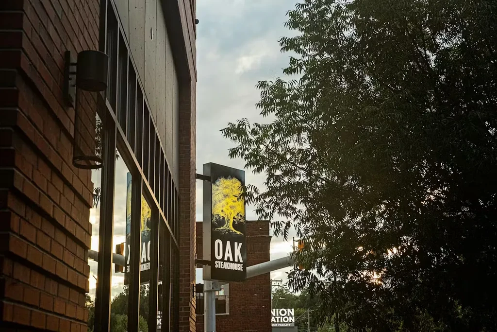 Oak Steakhouse sign with tree logo mounted on a brick building facade.