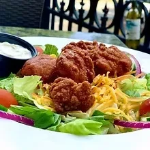 Plate of fried chicken salad with lettuce, cheese, tomatoes, and dipping sauce.