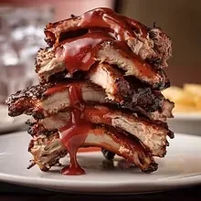 Close-up of stacked barbecued ribs with dripping reddish-brown sauce.