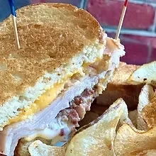 Cut grilled sandwich with turkey, cheese, bacon bits, and potato chips.