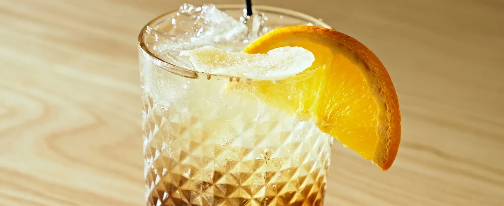 Faceted glass with two-toned drink, crushed ice, orange, and ginger garnish.