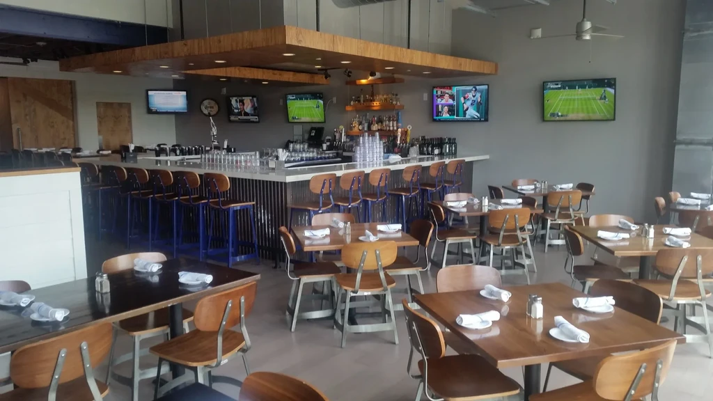 Bright, empty modern restaurant with bar, tables, and sports TVs.