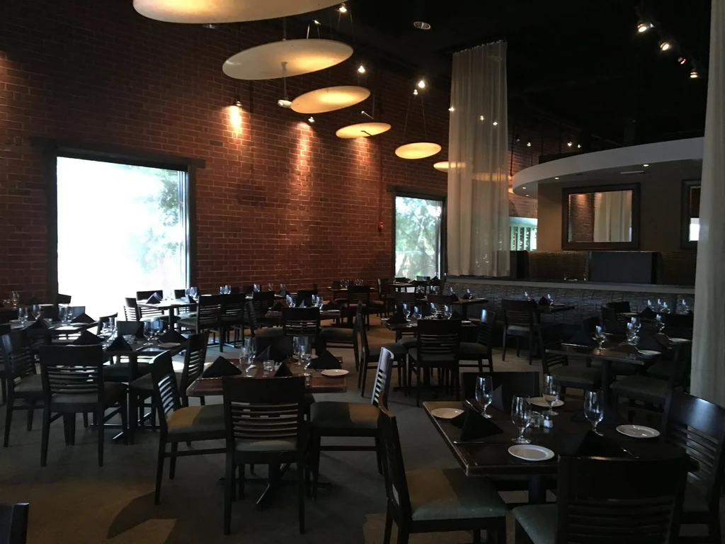 Restaurant dining room with brick walls, set tables, and warm interior lighting.