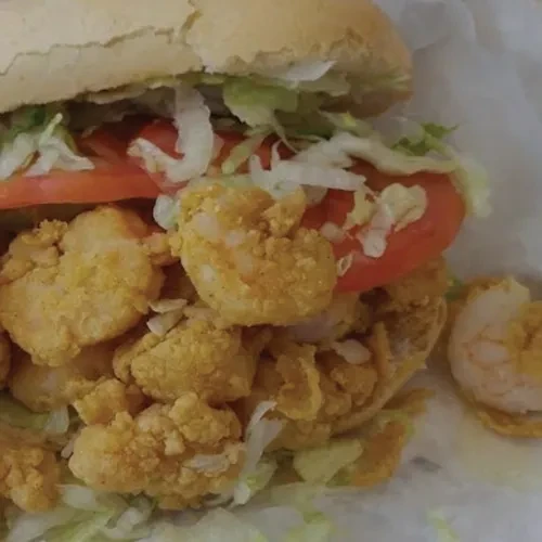 Close-up: fried shrimp sandwich with lettuce, tomato, and soft bread.