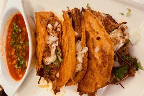 Birria tacos with consommé on a white plate, overhead view.