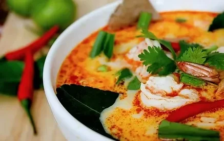 Vibrant steaming Tom Yum soup with shrimp, kaffir lime leaf, and herbs.