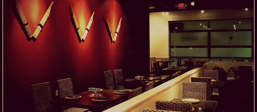 Dimly lit restaurant interior: red wall, bamboo V-decor, and set dining tables.