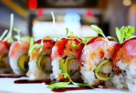 Platter of six inside-out sushi rolls with fish, sauce, and greens.