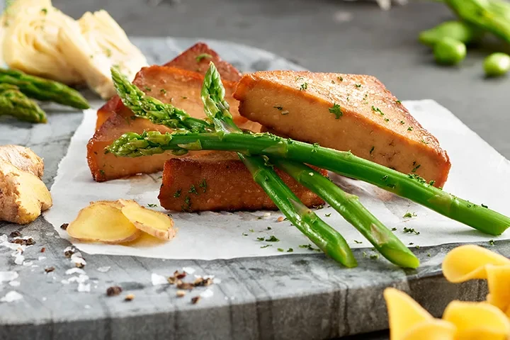 Rectangular protein with asparagus, ginger, and seasoning on a marble surface.