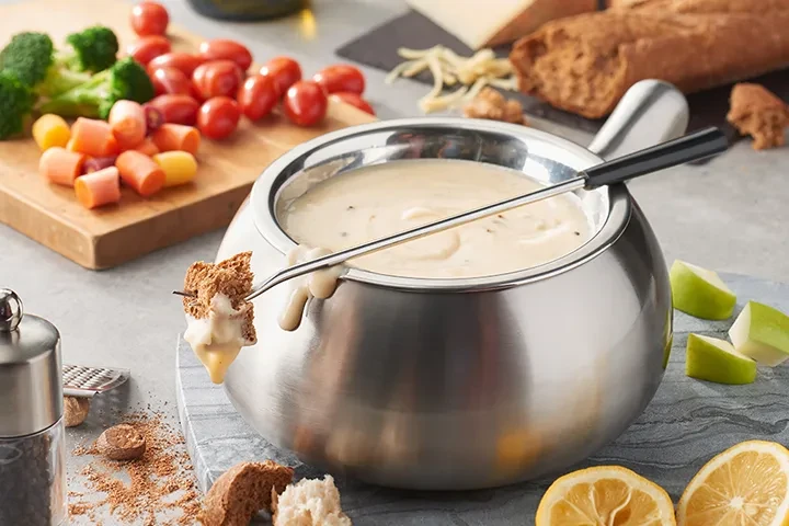 Fondue pot with fork dipping bread into cheese, surrounded by dippers.