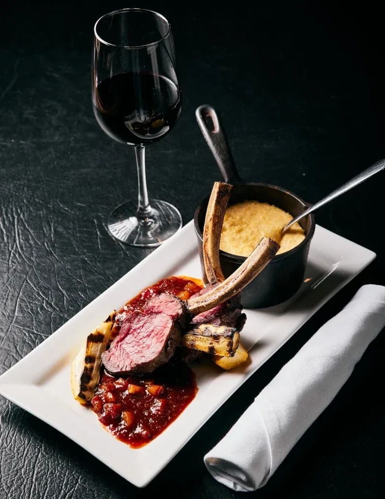 Plated lamb chops, red wine, creamy polenta, and roasted root vegetables.