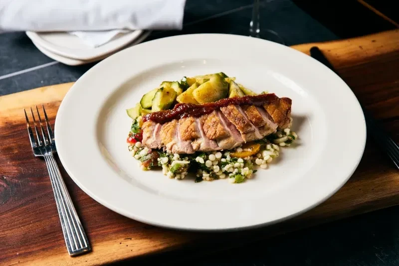 Sliced meat with couscous and cucumber salad on a white plate.