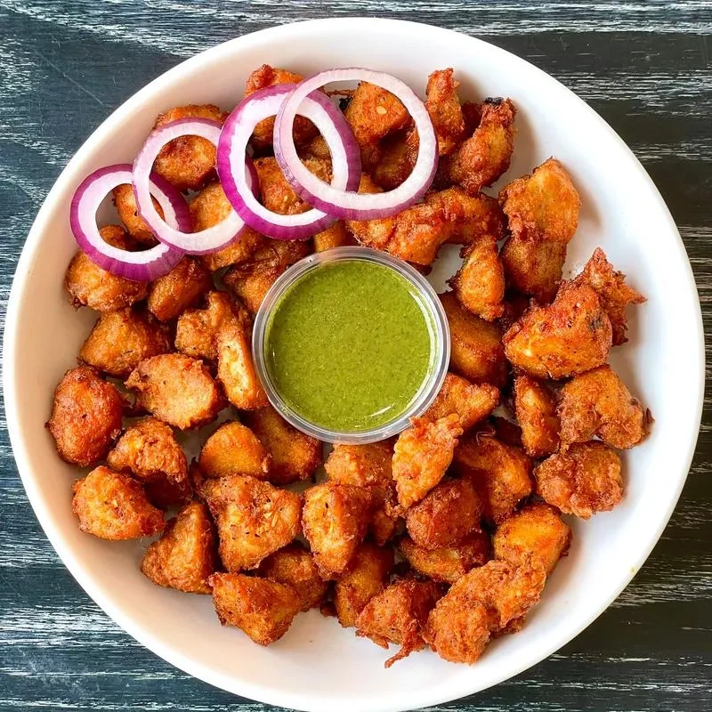 White oval bowl with crispy fried bites, green chutney, red onion.