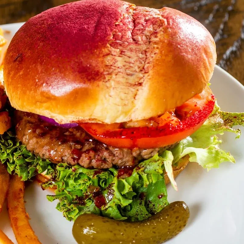 Close-up of a burger with a purple bun, fries, and dill pickle.
