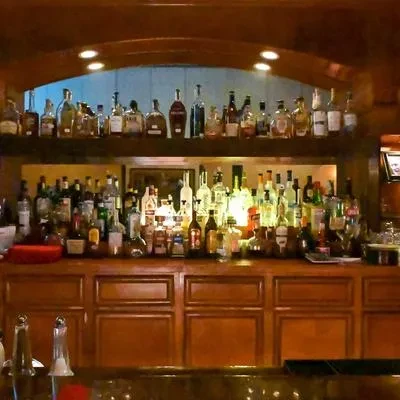 Warm, traditional wooden bar with many backlit liquor bottles on shelves.