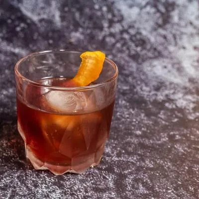 Old fashioned cocktail with spherical ice and orange peel.