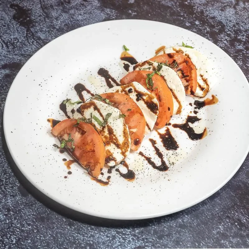 Close-up Caprese salad with tomato, mozzarella, basil, balsamic glaze.