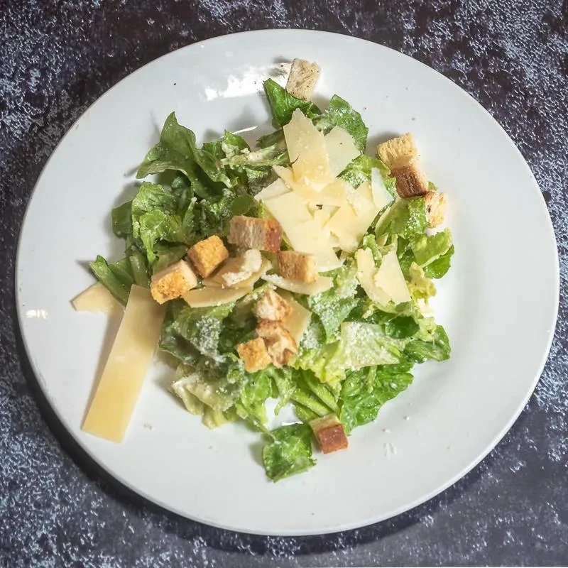 A Caesar salad with romaine, croutons, Parmesan, and white dressing.