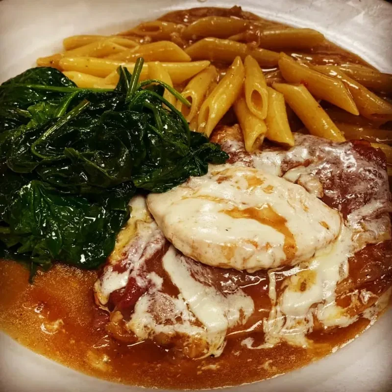 Overhead: Cheesy chicken, penne pasta, and spinach on a white plate.