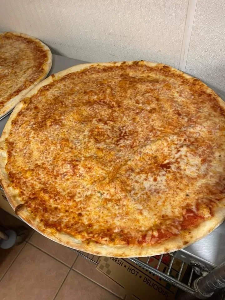 Two freshly baked cheese pizzas on a metal rack in a kitchen.