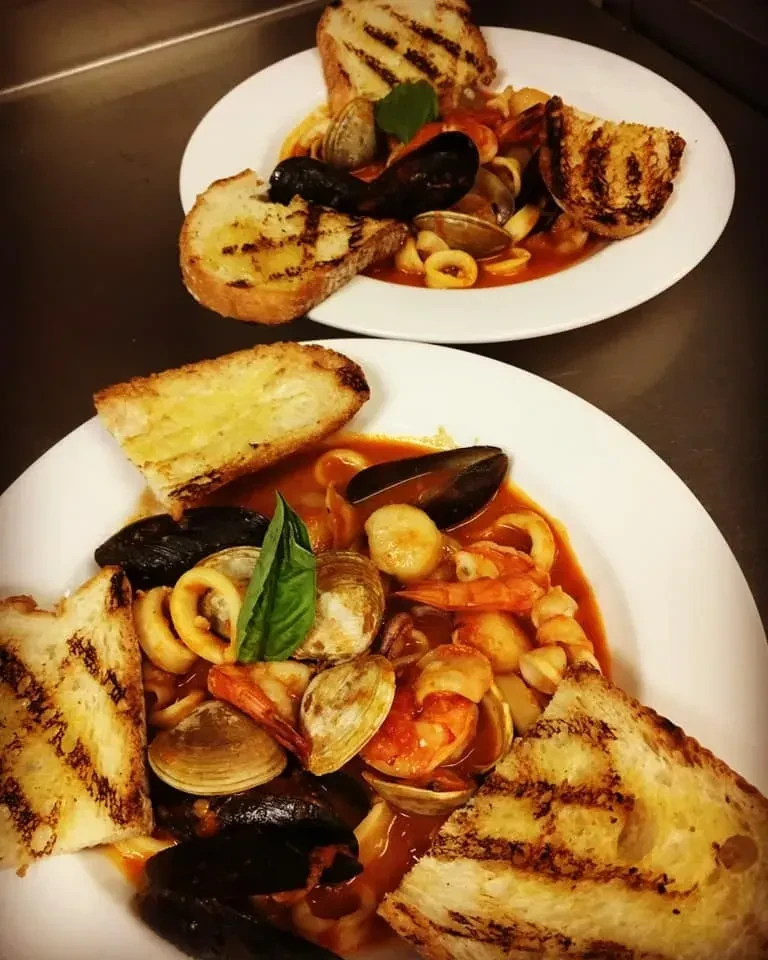 Two plates of seafood stew with mussels, shrimp, basil, and grilled bread.