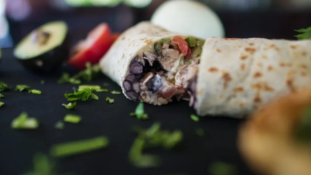 Cut burrito revealing fresh beans, protein, tomatoes, and avocado.
