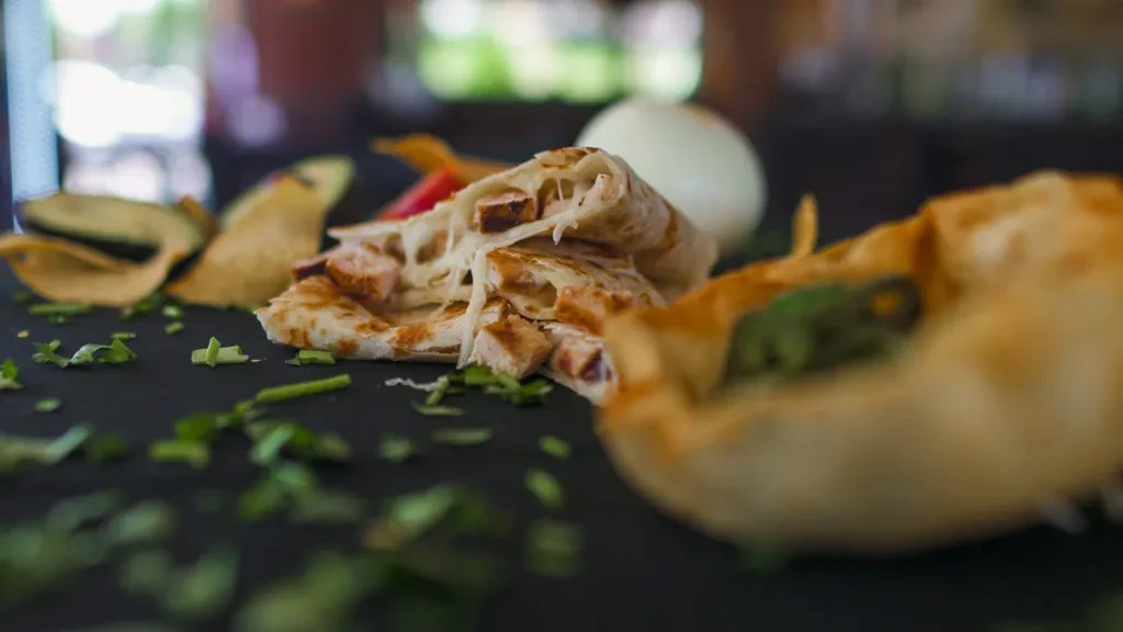 Low-angle close-up of cheesy meat quesadilla with avocado and chips.