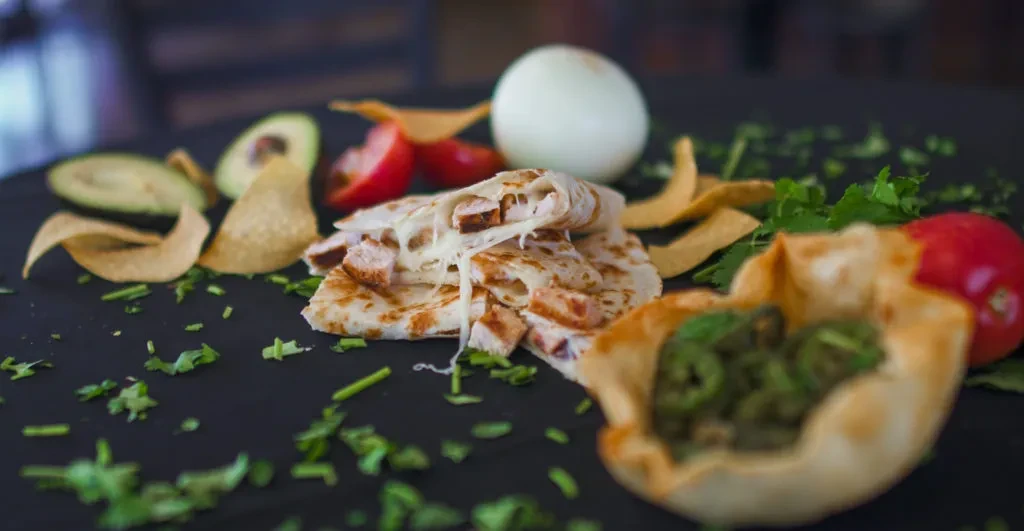 Stacked chicken quesadillas with melted cheese, avocado, tomato, and chips.