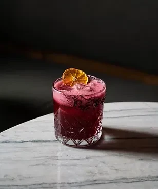Vibrant red-purple cocktail in textured glass with a dried orange slice.