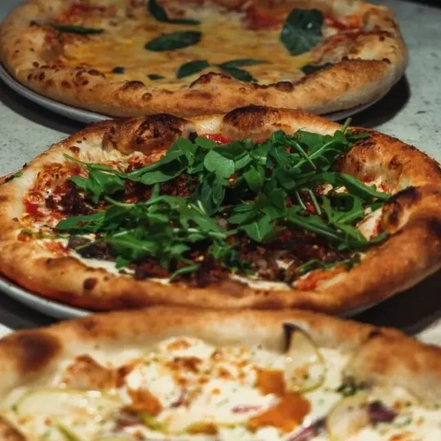 Three vertically stacked pizzas, the middle one topped with meat and arugula.
