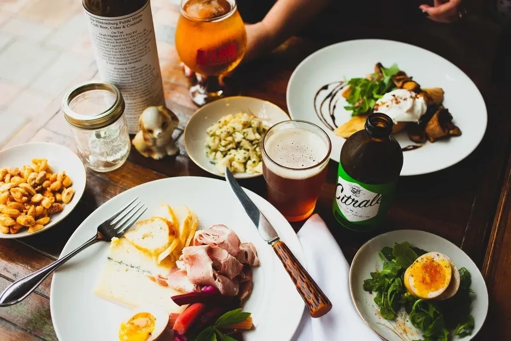 Overhead: charcuterie, roasted mushrooms, eggs, beer, and cocktails on wood.