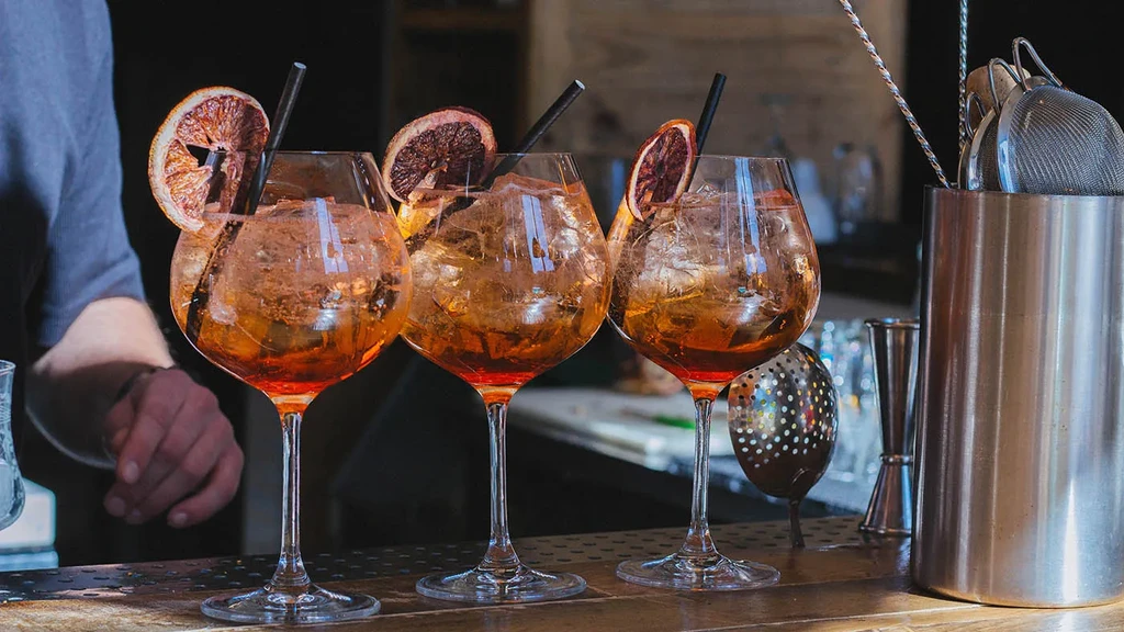 Three amber-orange cocktails with citrus and straws on a wooden bar.