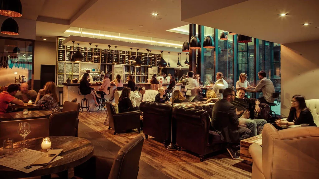 Warm, lively restaurant and bar interior with various seating and people.