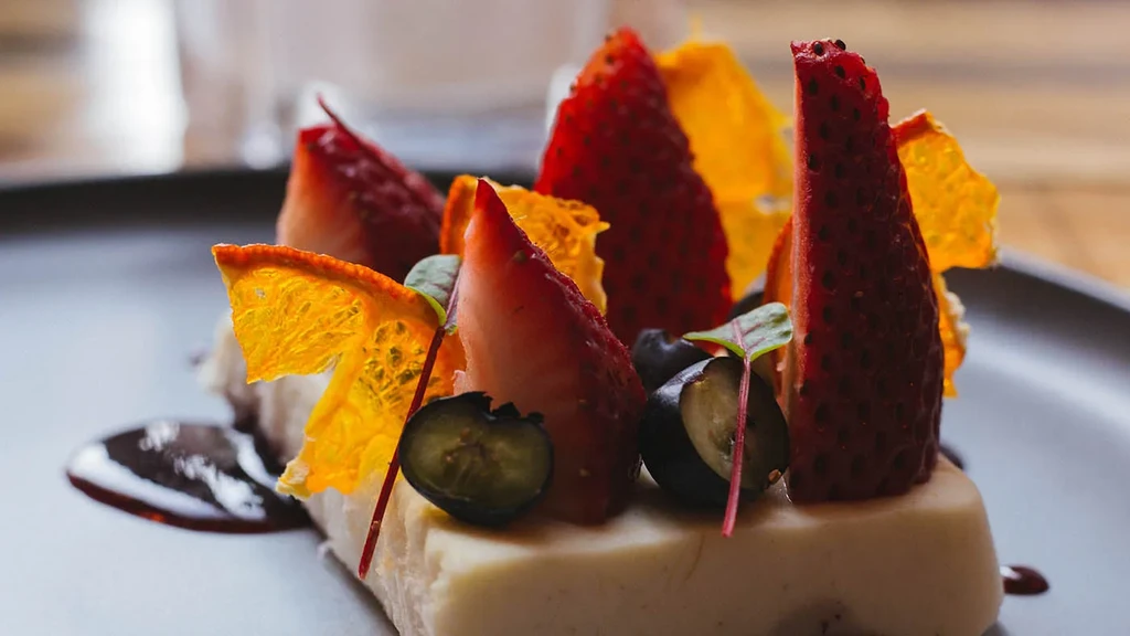 Creamy dessert with strawberries, blueberries, orange wafers, microgreens, and sauce.
