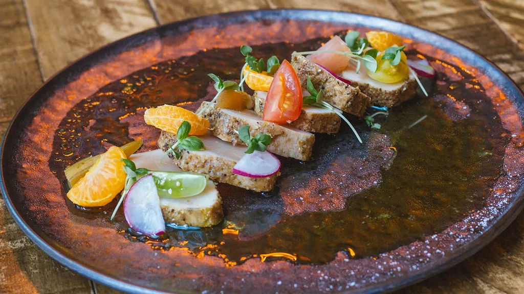 Seared protein slices plated with citrus, radish, tomatoes, and greens.