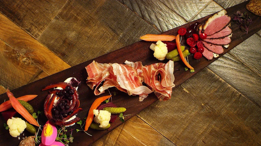 Rustic charcuterie board with meats, pickled vegetables, berries, and pink eggs.