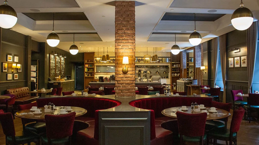 Empty upscale restaurant with brick column, red velvet booths, set tables.